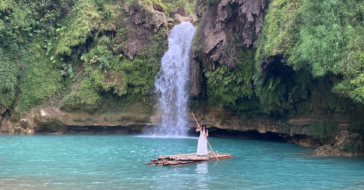 Raft trip down a river - Woman floating on raft with oar against waterfall