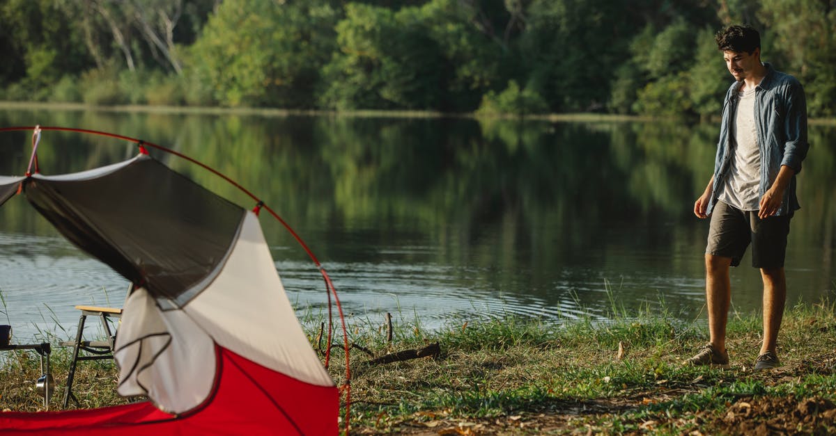 Raft trip down a river - Traveler on river shore against tent during summer journey