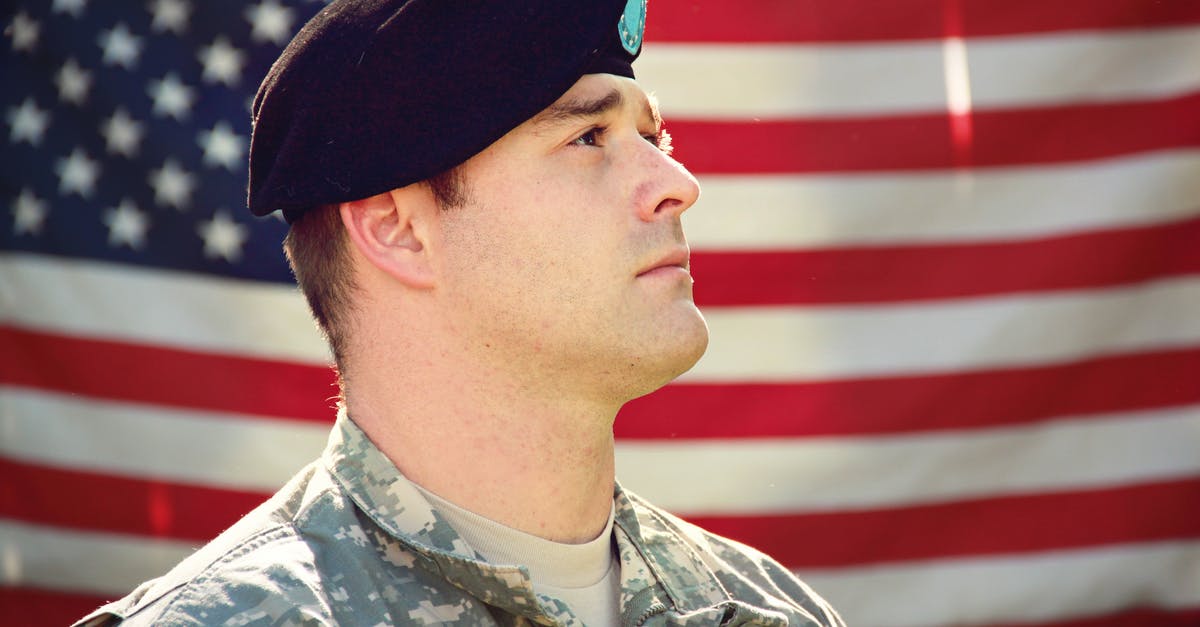 Rechecking checked in baggage when there's a stopover in the USA - Man Wearing Combat Hat And Top Looking Up Near Flag Of America