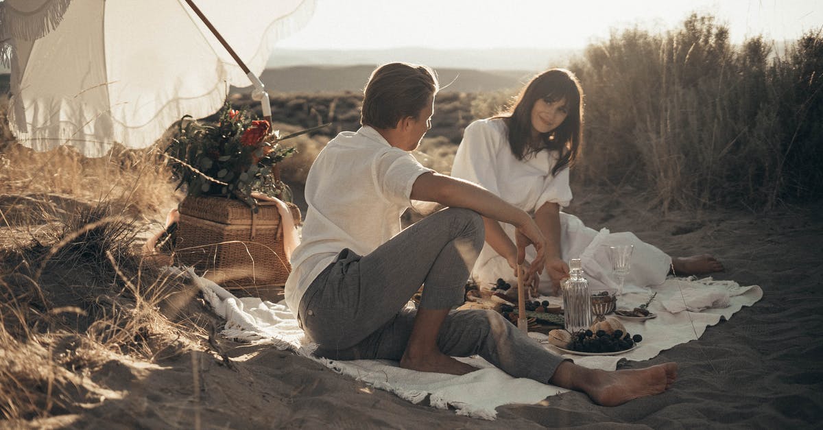 Re-entering the UK after our honeymoon [closed] - Young loving couple having romantic picnic sitting on white blanket with food and drinks under white umbrella