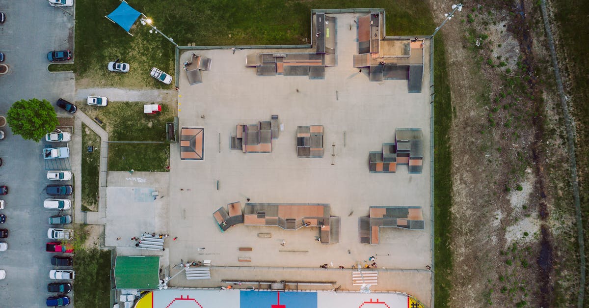 Re-entering the US on visa waiver from Mexico by car - Aerial view of skate park with various funboxes and ramps near inline hockey rink located in town near road with parked cars