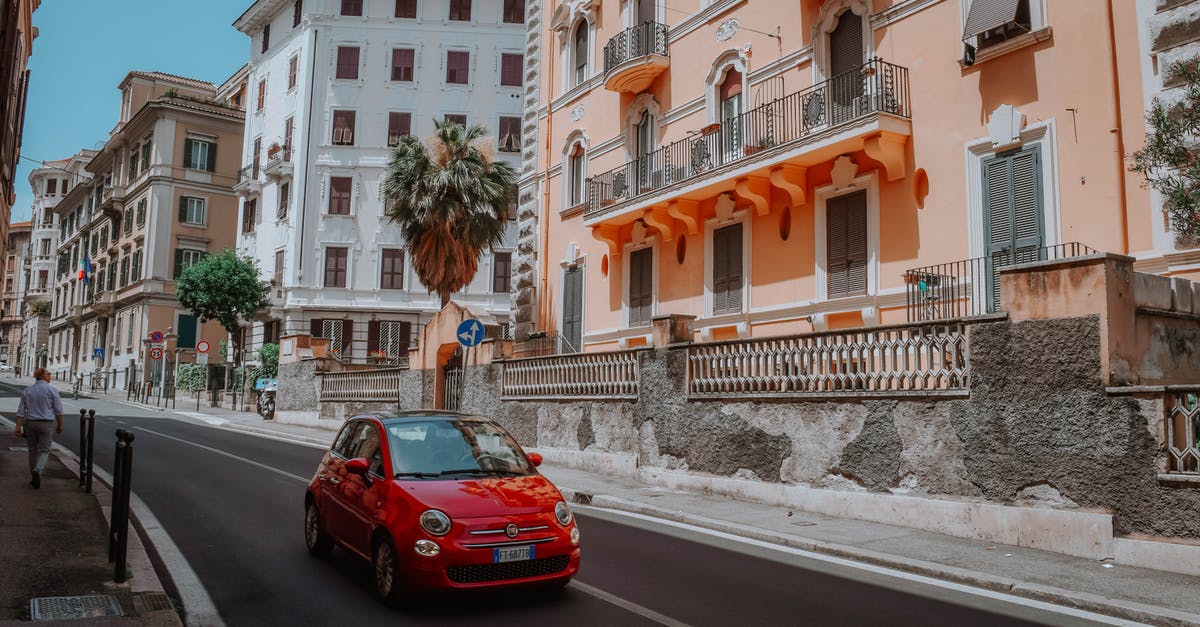 Rent a car for a day and leave it in another city in Italy - Red 5-door Hatchback On A Narrow Street Lined With Apartment Buildings