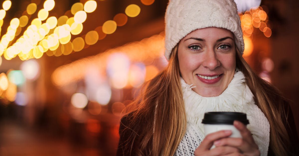 Rent clothing in Frankfurt / Being warm without cold weather clothing - Cheerful female in warm outerwear standing with beverage to go on street and chilling during weekend in evening in city illumination while looking at camera