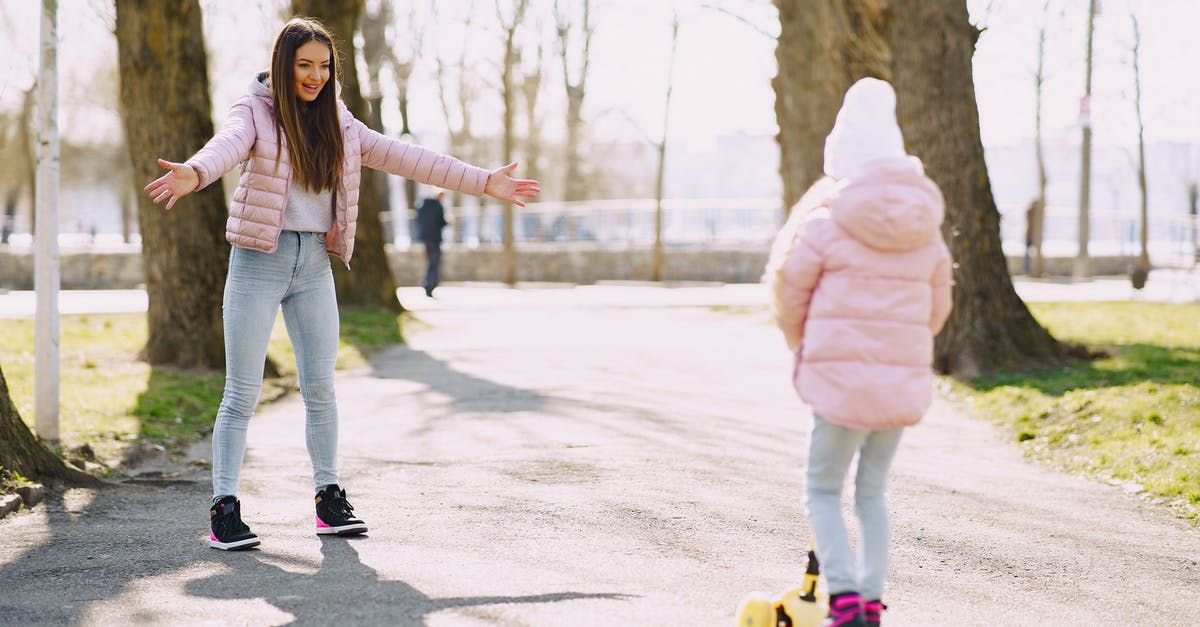 Rentalcars full coverage insurance - Full body little girl riding kick scooter on alley in park while mother standing with hands apart for support in sunny day