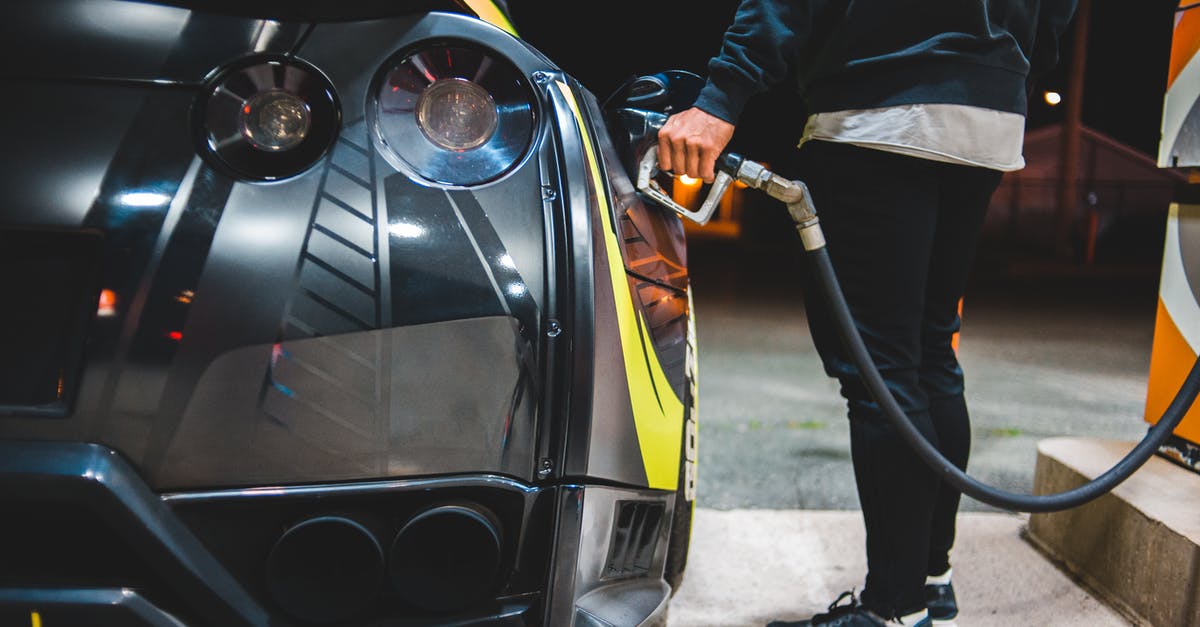 Rented car in Switzerland: fuel and gas station - Side view of crop unrecognizable male refueling modern racing automobile in petrol station in evening