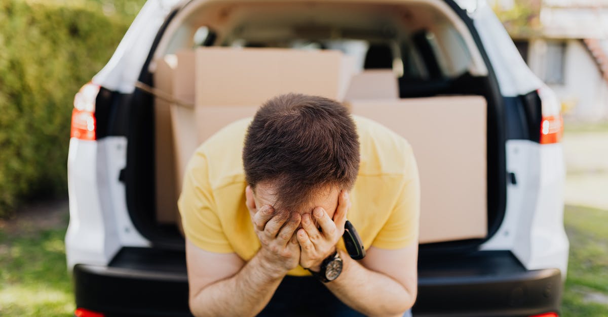 Renting a car - Slovakia - Faceless frustrated tired male wearing casual outfit sitting on car luggage boot and covering face with hands during relocation on sunny summer day