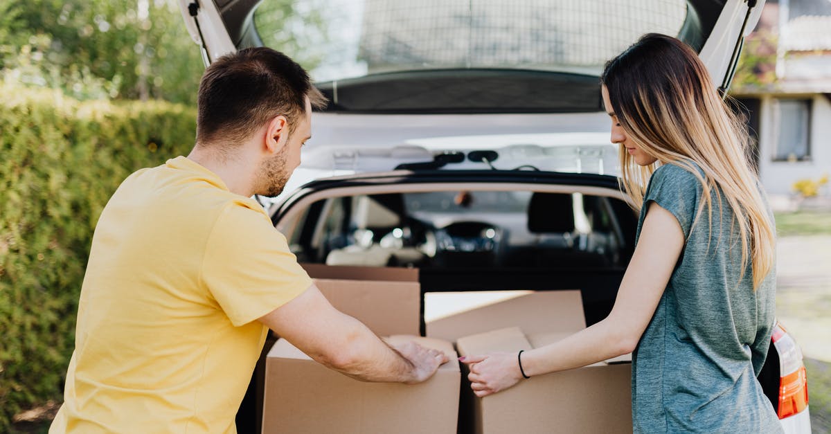 Renting a car - Slovakia - Calm couple putting carton boxes into car trunk