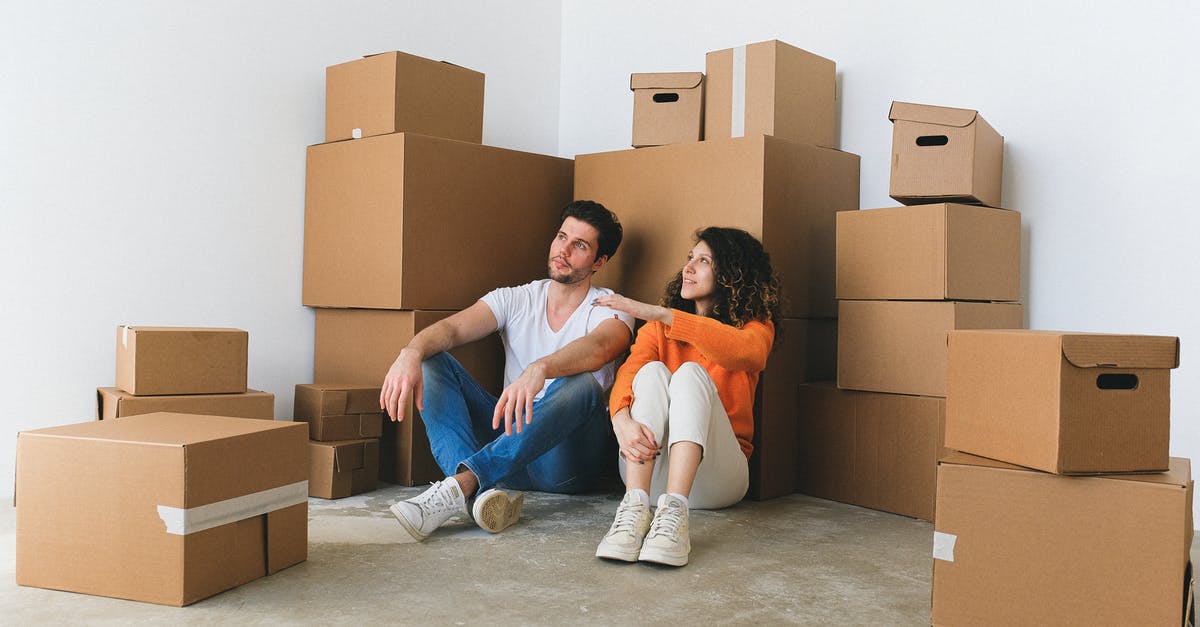 Renting a flat in Montenegro [closed] - Full body of young happy couple in casual clothes sitting on floor leaning on stack of cardboard boxes and chatting after relocation in new flat