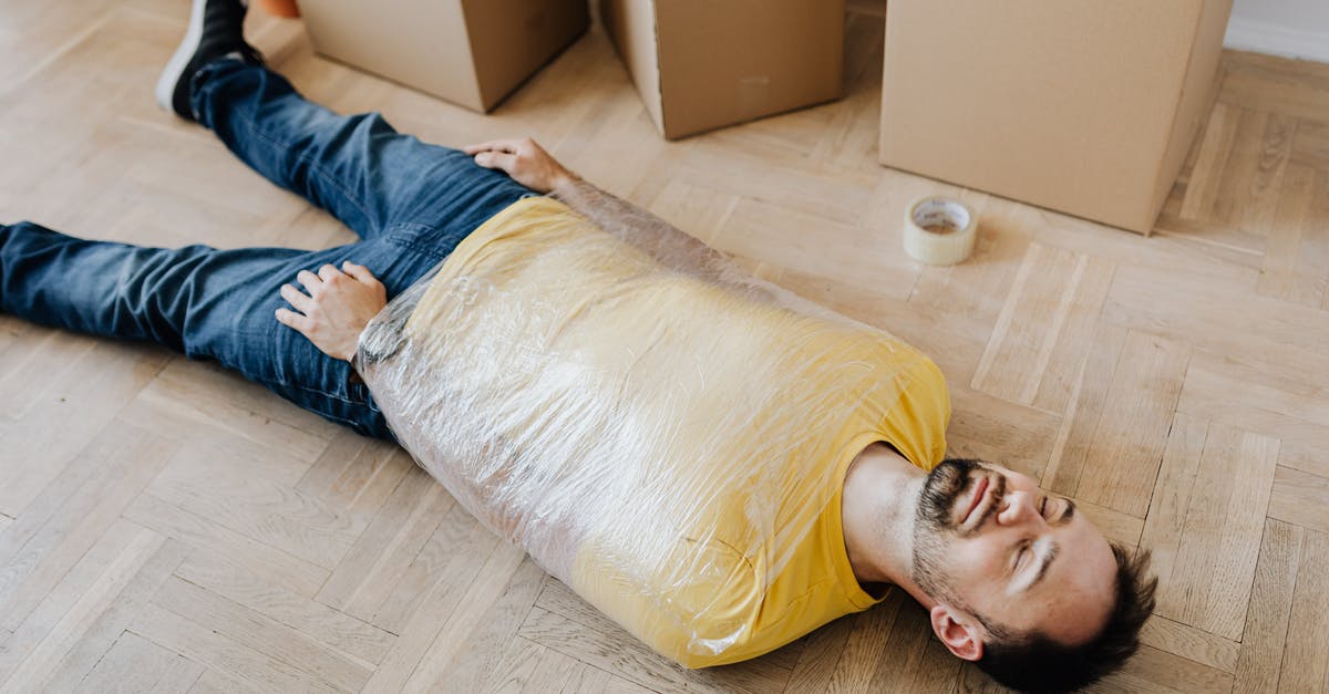 Renting a flat in Montenegro [closed] - High angle of tired male in casual wear wrapped in plastic tape and lying on parquet with eyes closed near carton boxes during relocation