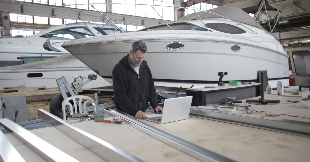 Required to check-in in person at international layover airport - Adult worker using laptop at workbench during work in boat garage