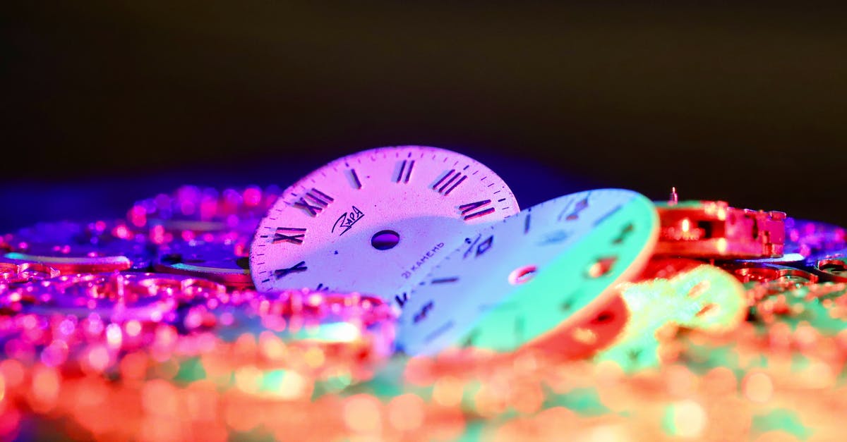 Reservation for multiple room in hotel - different check-in time - Round clock faces with Roman and Arabic numerals placed among stack of watch movements in dark room on black background