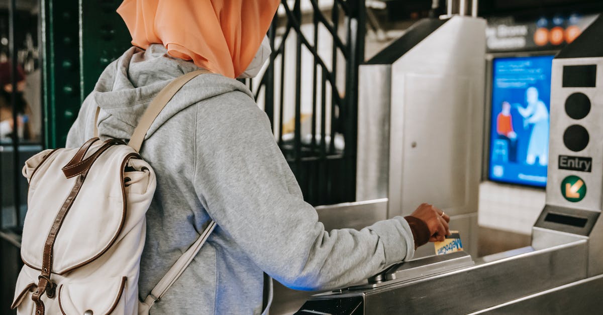 Residence permit card in Finland sent while travelling back to U.K - Back view Muslim woman in casual outfit and hijab with backpack using travel card for passing metro gate at daytime