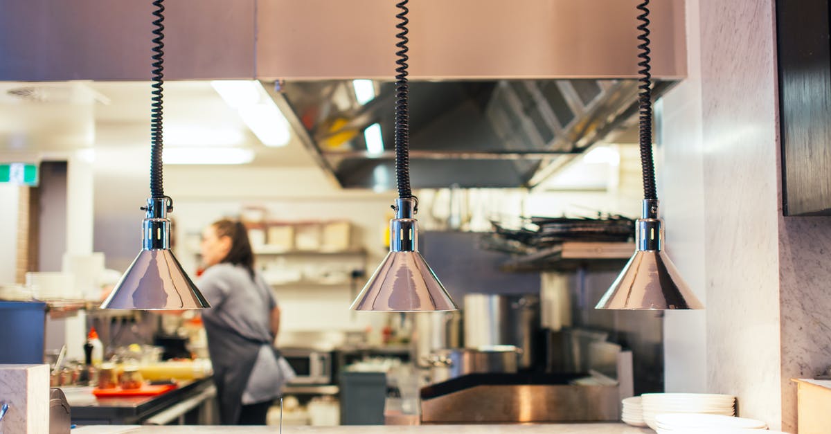 Restaurant in Paris decorated in kitchen utensils - Side view of unrecognizable female chef in restaurant kitchen working behind counter with infrared lamps and serving kitchenware