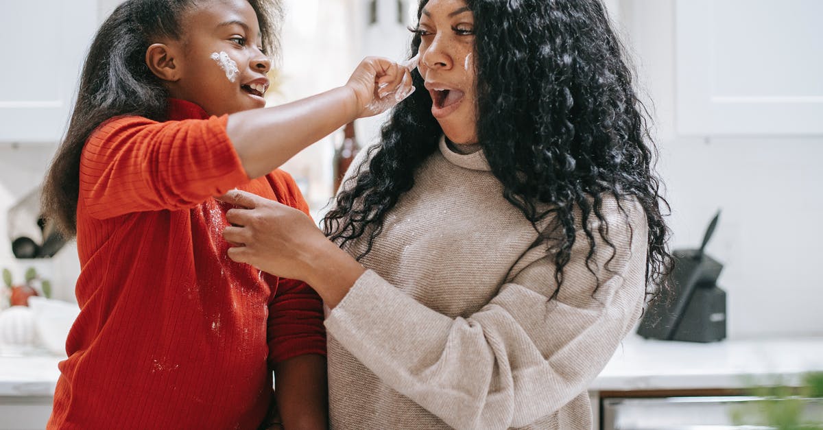 Retired Parents - Apply Visitor Visa - Positive dirty ethnic child applying flour on face of young crop parent while having fun in kitchen and looking at each other