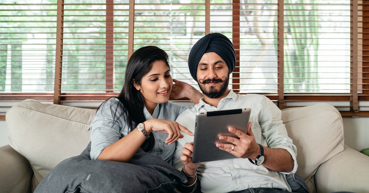 Revealing relationship on German visa application - Content Indian woman and man in turban resting on cozy couch in living room and sharing tablet