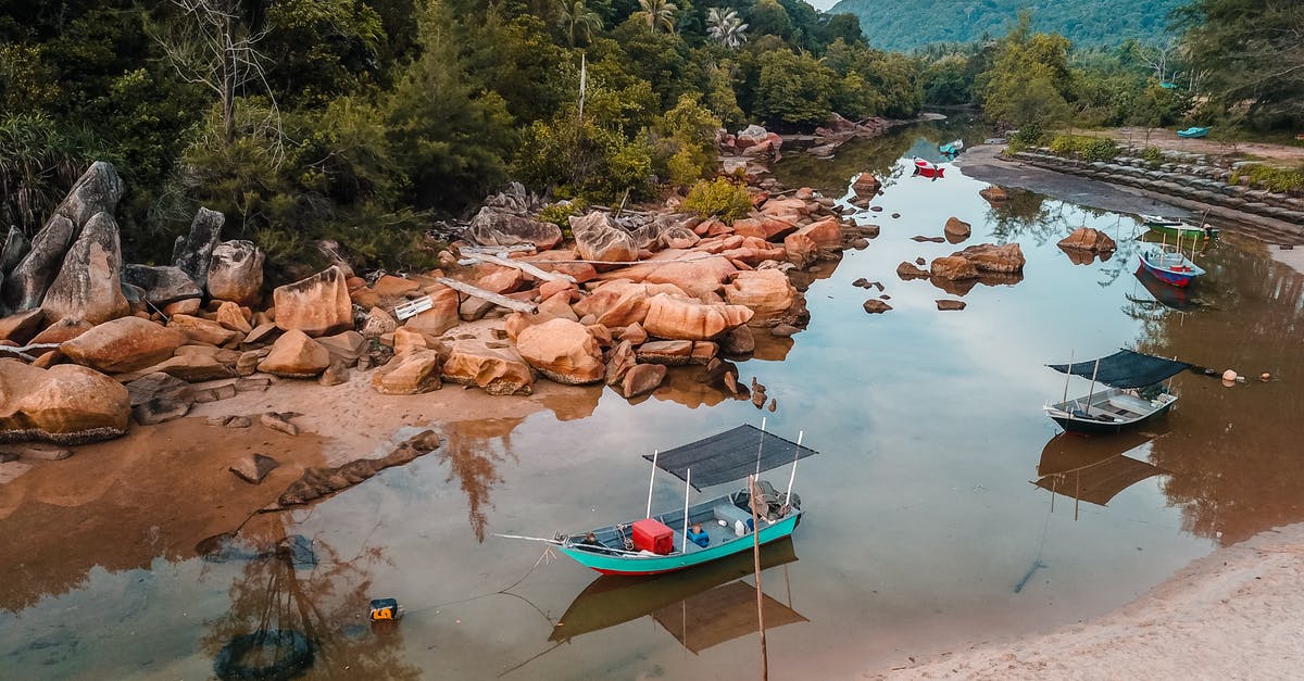 Rocky beach accessible from Faro by public transport [closed] - From above of boat moored on rocky sea shore under tropical forest with green plants in daytime