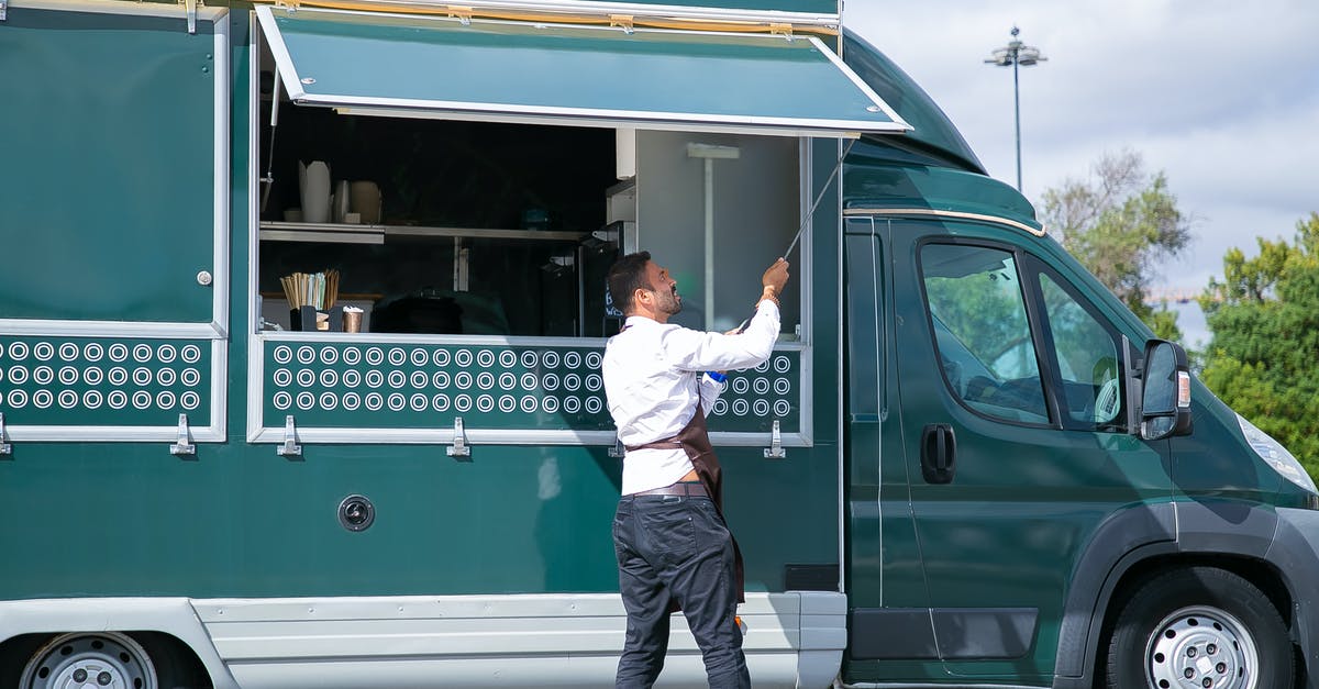 Roland-Garros (French Open) public viewing in Paris? - Side view young waiter in apron standing outside food truck and opening counter door in green lush park