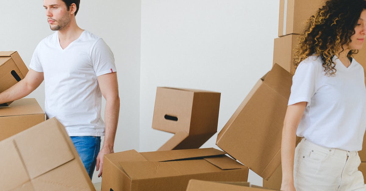 Rolling shirts in a bundle VS laying them flat while packing? - Serious young man and woman in white t shirts carrying carton boxes in light room while moving into new apartment together