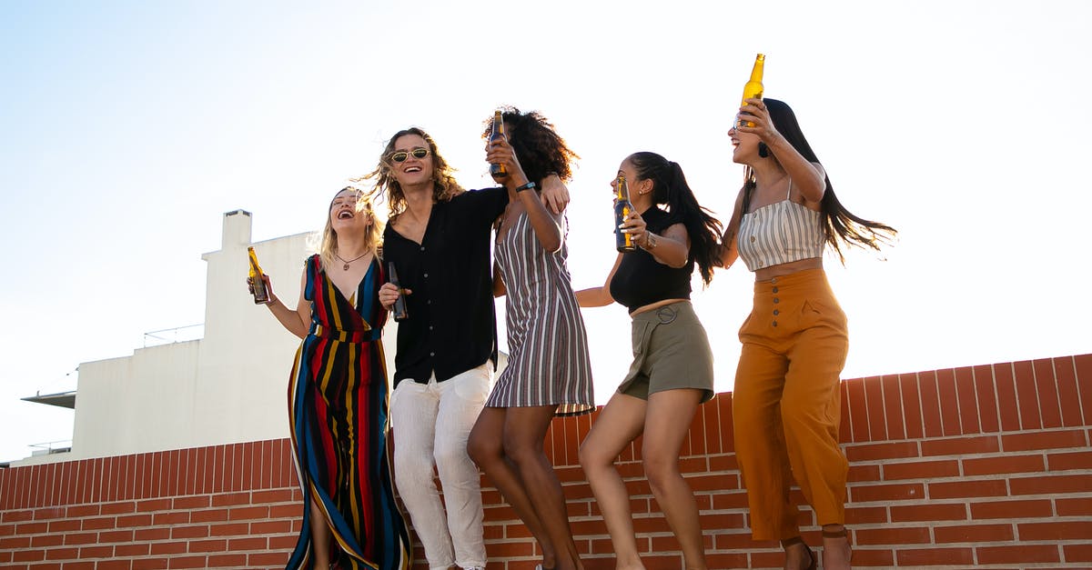 Rooftop Bars in Jakarta [closed] - Low angle full body of multiracial friends having party with raised arms while celebrating together and drinking beer on rooftop