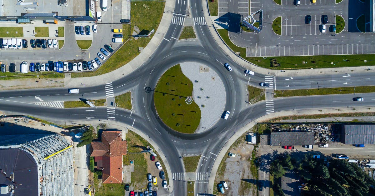 Roundabout in left drive countries - Drone view of roundabout at intersection of asphalt roads near modern buildings and parked cars in city district on sunny day