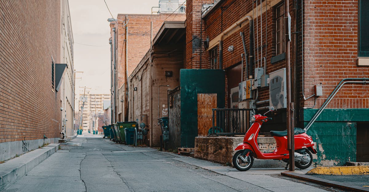 Route planner for moped in Norway and Sweden? - Aged house facades with shabby brick walls between empty asphalt roadway with cracks and parked moped under sky in town