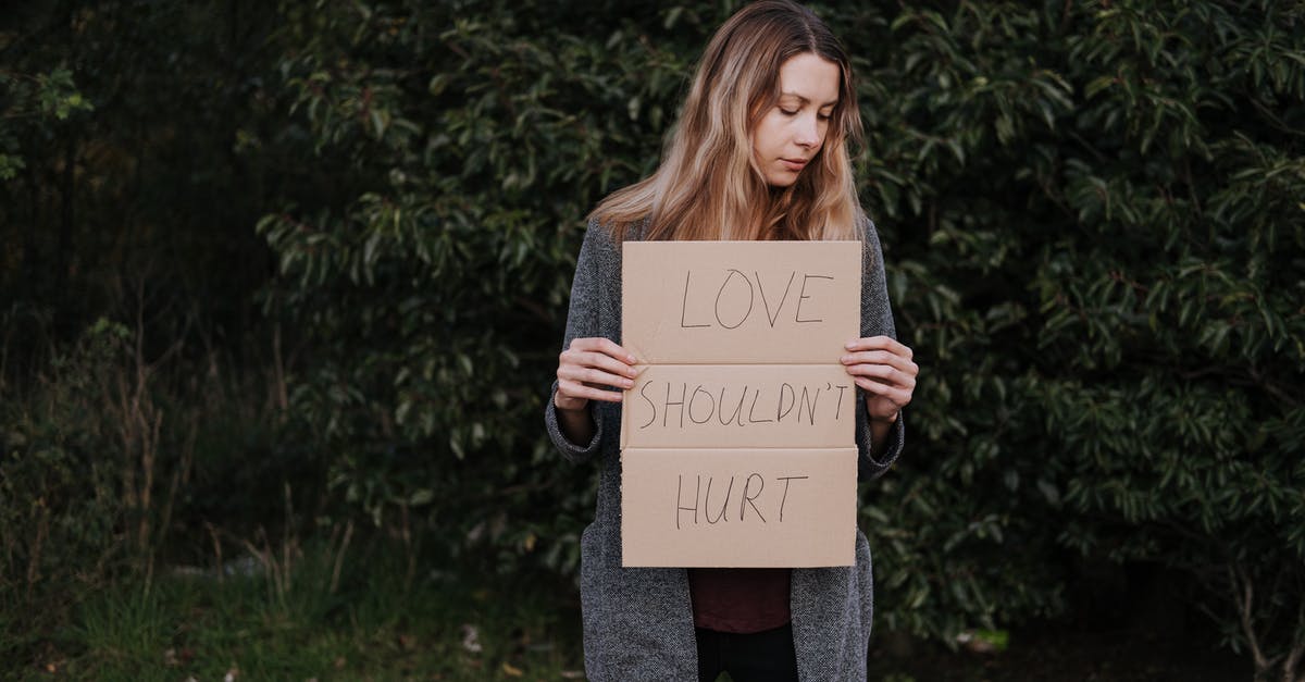 Safeguarding against extra expenditures Natural disasters during travels - Lonely upset female in casual outfit standing near trees and grass while holding cardboard against abuse with inscription Love Should Not Hurt