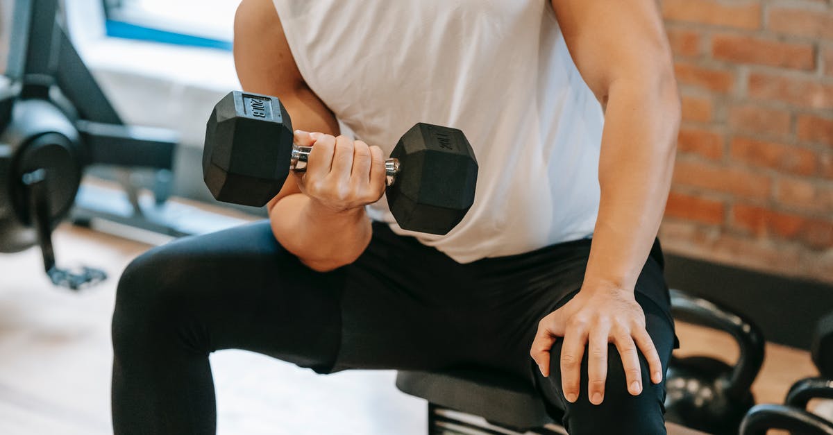 Scared that I won't fit in plane seat [duplicate] - Unrecognizable strong male pumping bicep while lifting heavy metal dumbbell in modern fitness studio with sportive equipment near brick wall