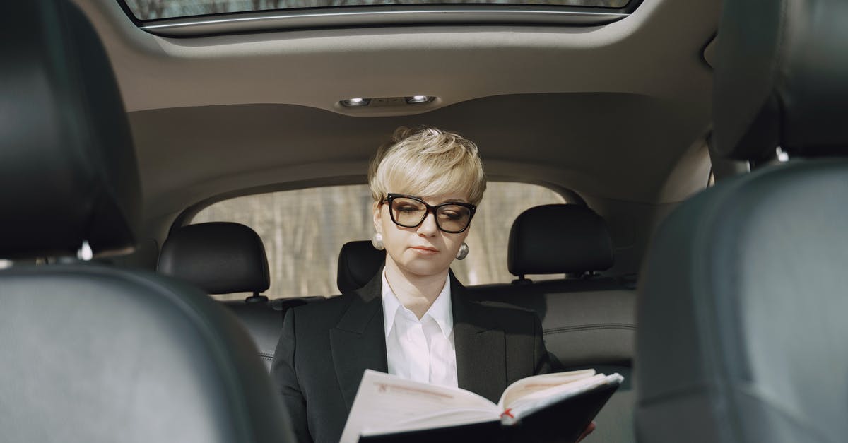 Scheduling a ride with Uber - From below of concentrated female entrepreneur in elegant formal clothes sitting on backseat while reading memos in notebook riding in car