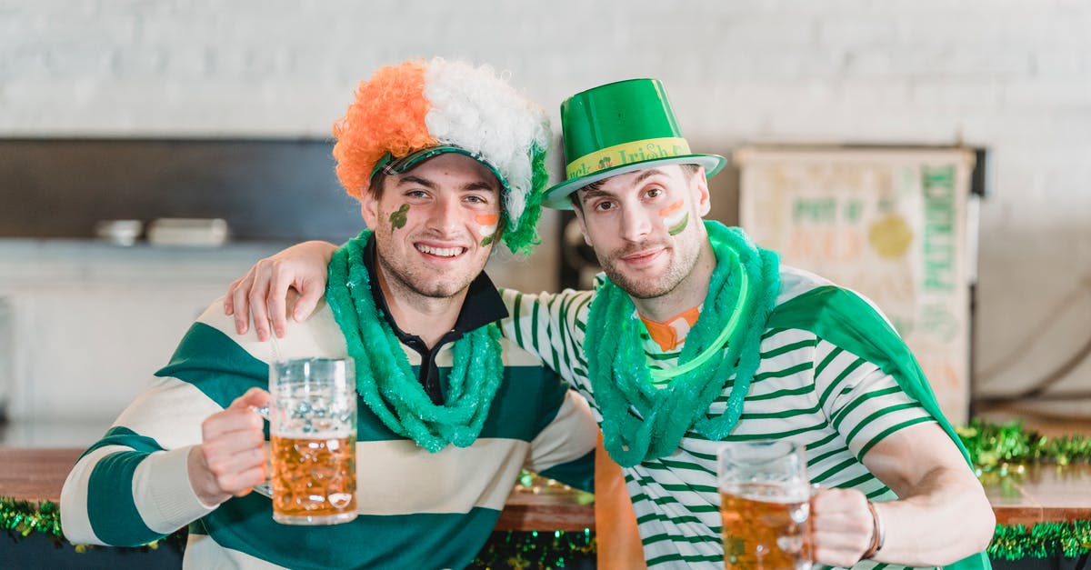 Schengen days and Ireland - Happy young male friends in traditional green and yellow outfits and hats cuddling and smiling while drinking cold beer during St Patricks Day celebration in pub