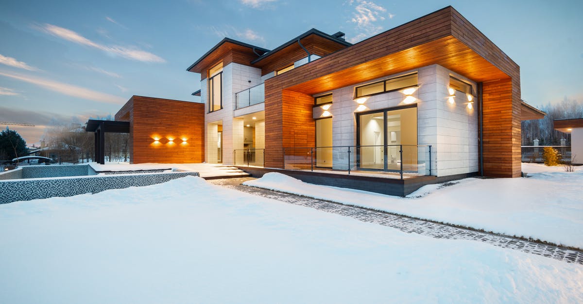 Schengen visa - Change of location - Exterior architecture of private suburban cottage house with stone and wooden facade and large windows overlooking spacious snow covered yard in winter day