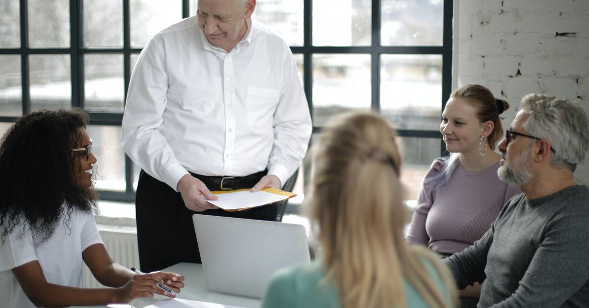 Schengen visa documents if the job is just 2 month old - Positive multiracial colleagues of different ages gathering at table in modern workspace while old man presentation project