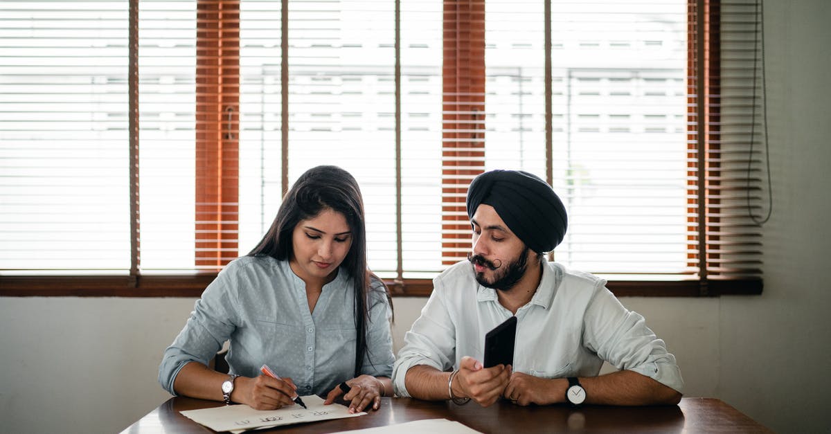 Schengen visa for an Indian student in Ireland - Indian woman with papers and pen writing on paper poster with ethnic Indian man in turban sitting nearby at wooden table