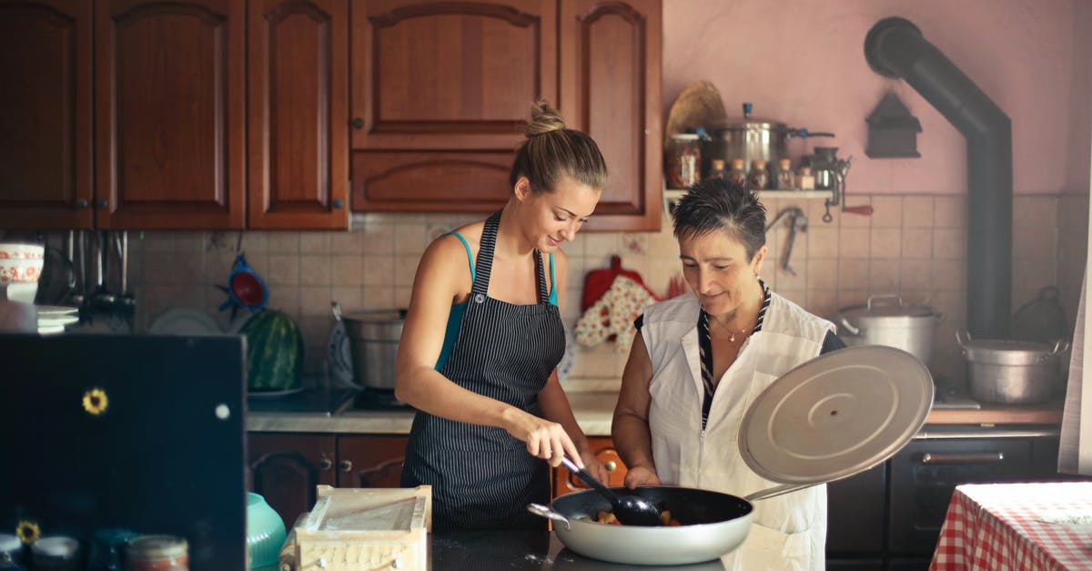 Schengen visa for housewife - Daughter and senior mother standing at table in kitchen and stirring dish in frying pan while preparing food for dinner