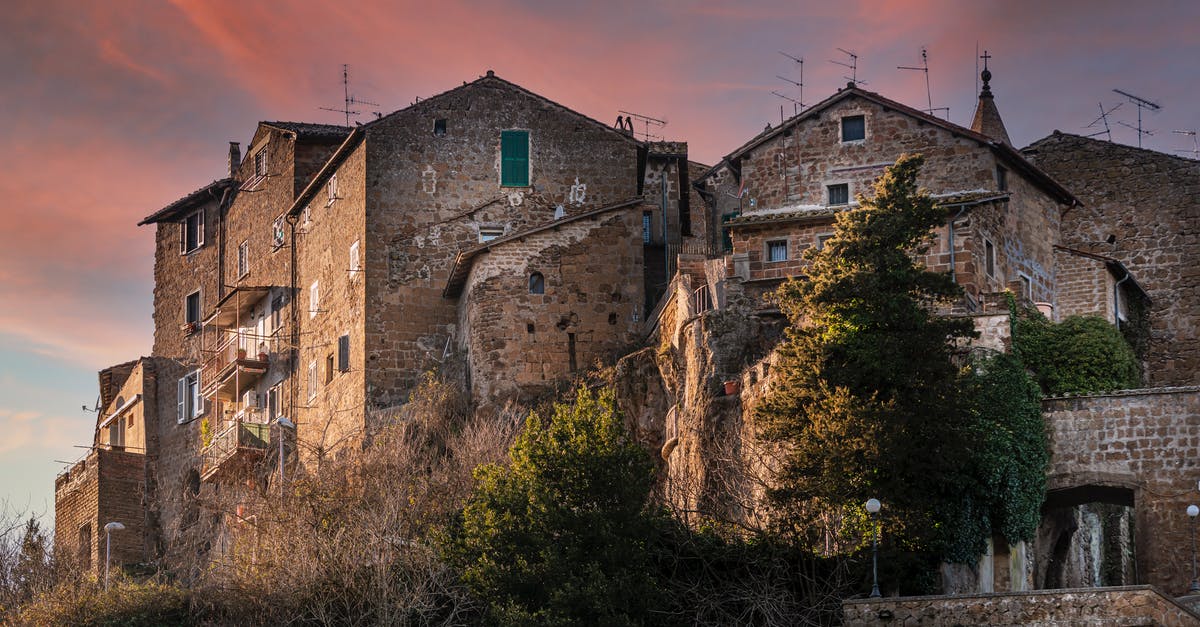 Schengen visa from Italy without visiting Italy - From below of aged stone houses of Calcata medieval town located on hill top under amazing sundown sky