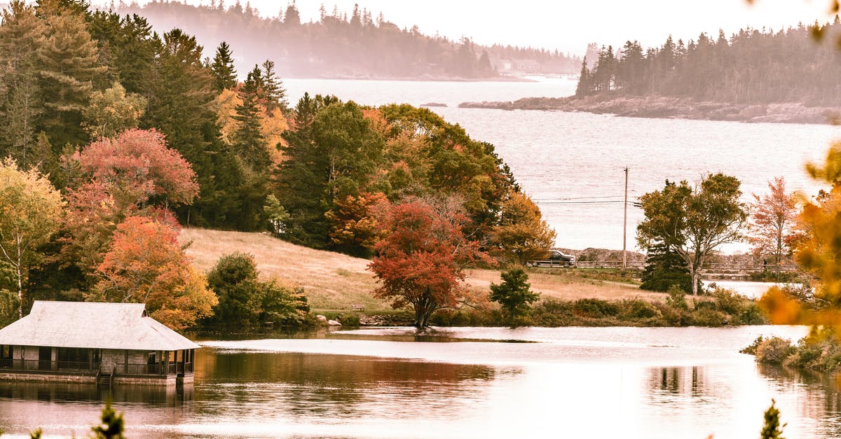 Schengen visa main country for a mix of tourism/family visits - Breathtaking view of rural house located on tranquil river streaming between colorful bright red and yellow trees on autumn day