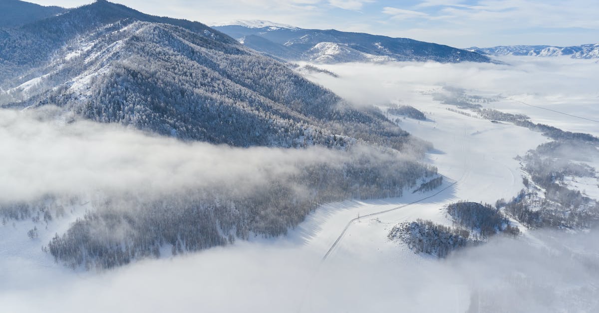 Schengen visa through VFS in India: No update for 20 days - Drone view of snowy valley among mountains covered coniferous forest and road going between mountain ridge through clouds in sunny winter day