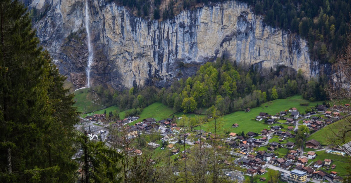 Schengen visa to travel from Germany to Switzerland - From above of picturesque rocky mountain covered with coniferous trees with waterfall flowing above small village of Lauterbrunnen in Switzerland