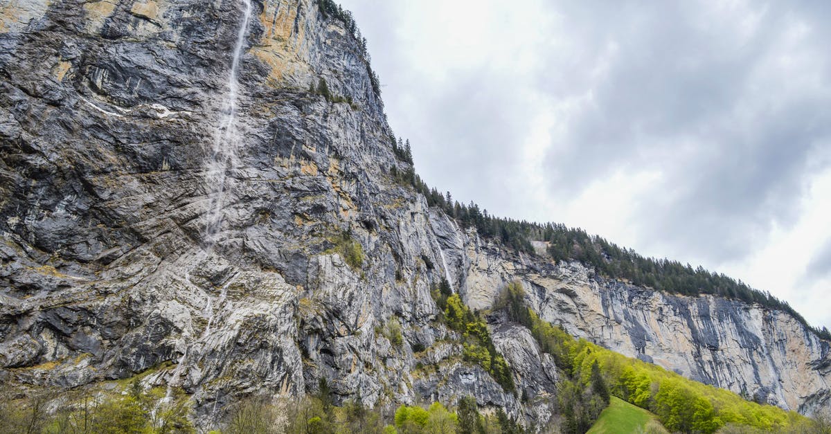 Schengen visa to travel from Germany to Switzerland - Rocky mountain ridge with flowing waterfall and green vegetation on cloudy day in Switzerland