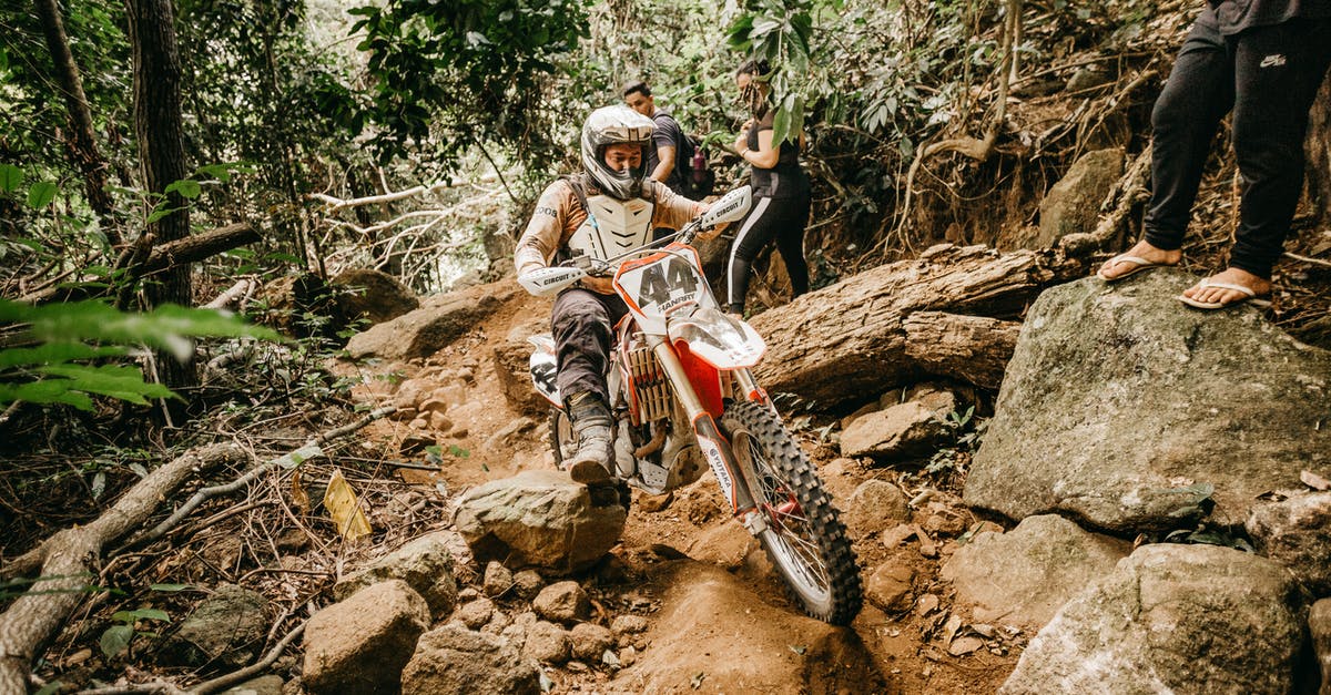 Search engine for bicycle rentals - Energetic male biker in helmet riding mountain motorbike on rough stony terrain in tropical forest