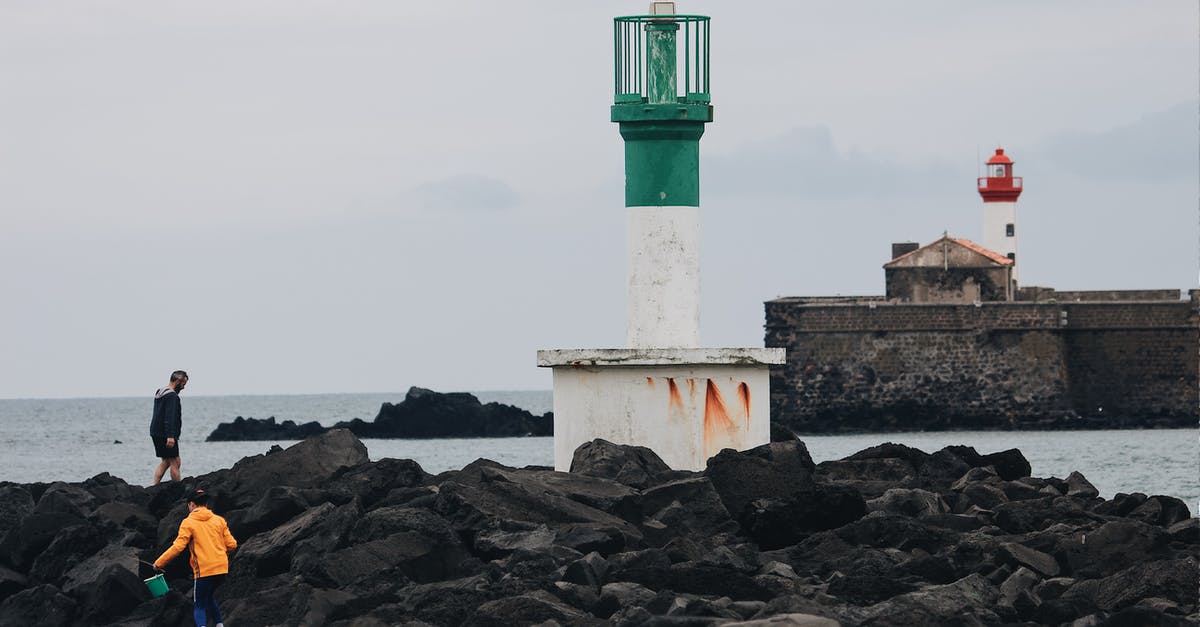 Security situation along I-75 on Florida's Gulf Coast - Unrecognizable people walking on rough stony breakwater with lighthouse tower in gray overcast weather  on seashore