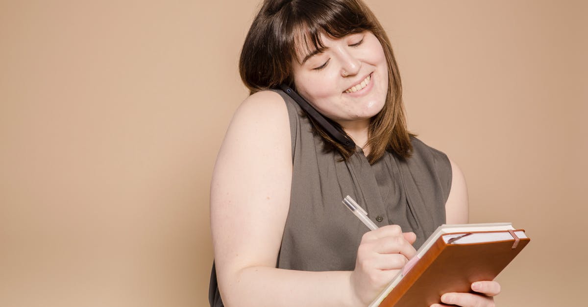 Send 1 overweight suitcase instead of 2 underweight? - Cheerful Asian woman writing in notebook while having phone call