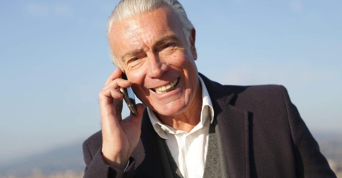 Senior aged travelers - Delighted male entrepreneur wearing classy jacket standing in city and making phone call while smiling and looking at camera