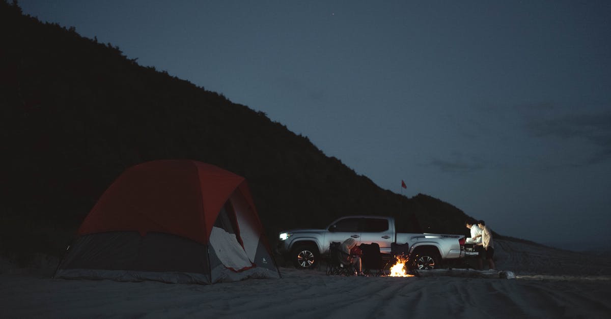 Setting up a tent on a beach in Greece - Anonymous tourists on sandy beach with pick up and burning bonfire near camping tent in night time in nature during campaign