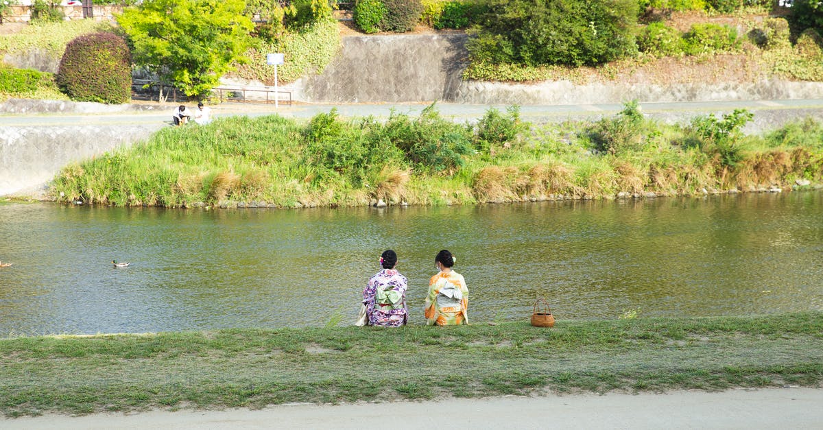 Shore Pass at Narita Airport, Japan - Back view of anonymous ethnic women in traditional kimono apparels contemplating rippled river from coast in town