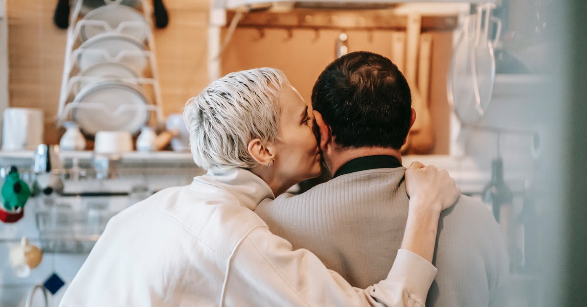 Short Stay Schengen Visa for non Eu spouse - Back view of happy adult woman with short blond hair in casual clothes kissing cheek of anonymous husband while standing together in kitchen