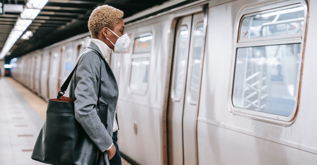 Short transit in ZRH, will I have enough time? - Side view of unrecognizable confident young black female entrepreneur with short blond hair in elegant outfit and face mask standing in front of train in metro station