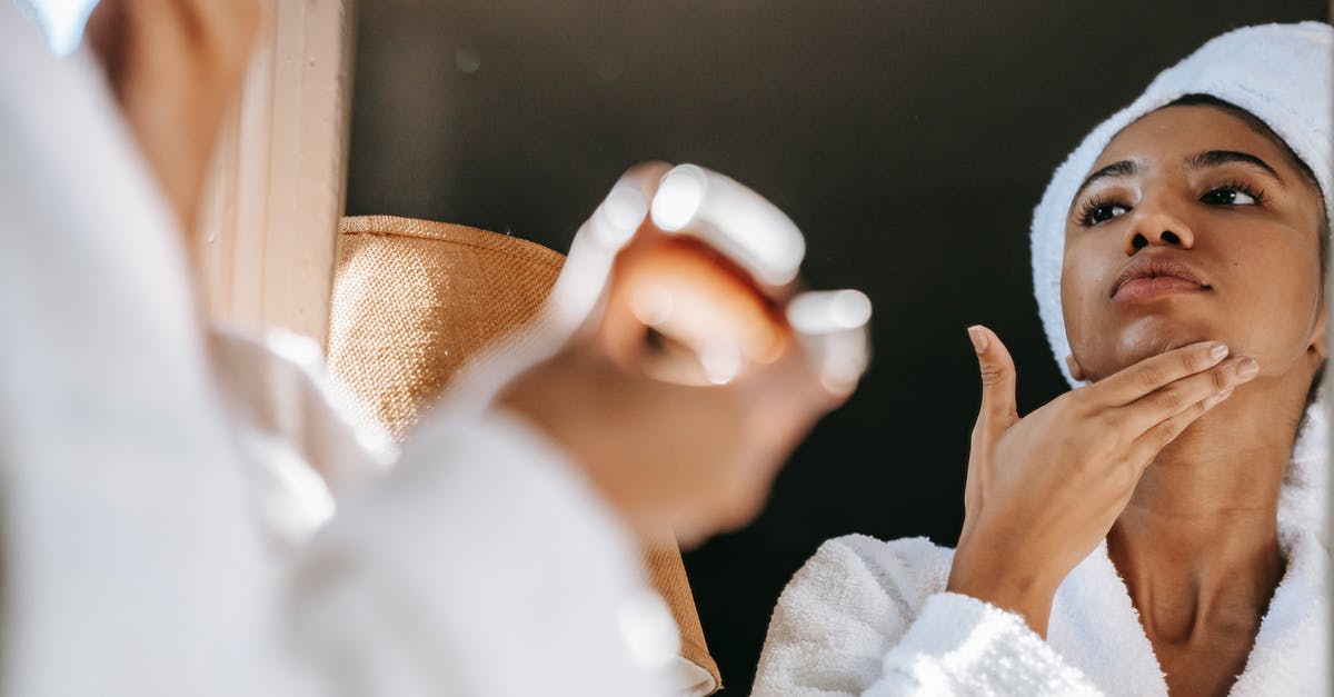 Should I bring sufficient anti-mosquito lotion to China? - African American young female in white bathrobe applying moisturizing cream on face while standing in bathroom
