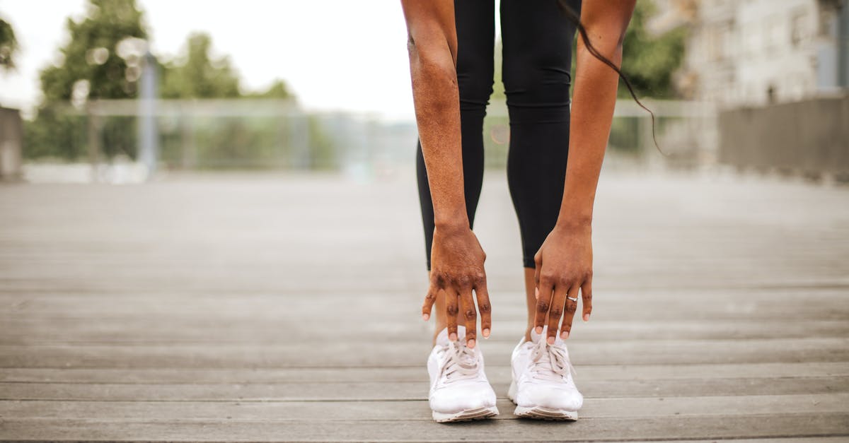 Should I travel to Morocco alone as a young female? - From below crop slender female athlete in sportswear and white sneakers doing standing forward bend exercise for stretching body on wooden floor of street sports ground against blurred urban environment in daytime