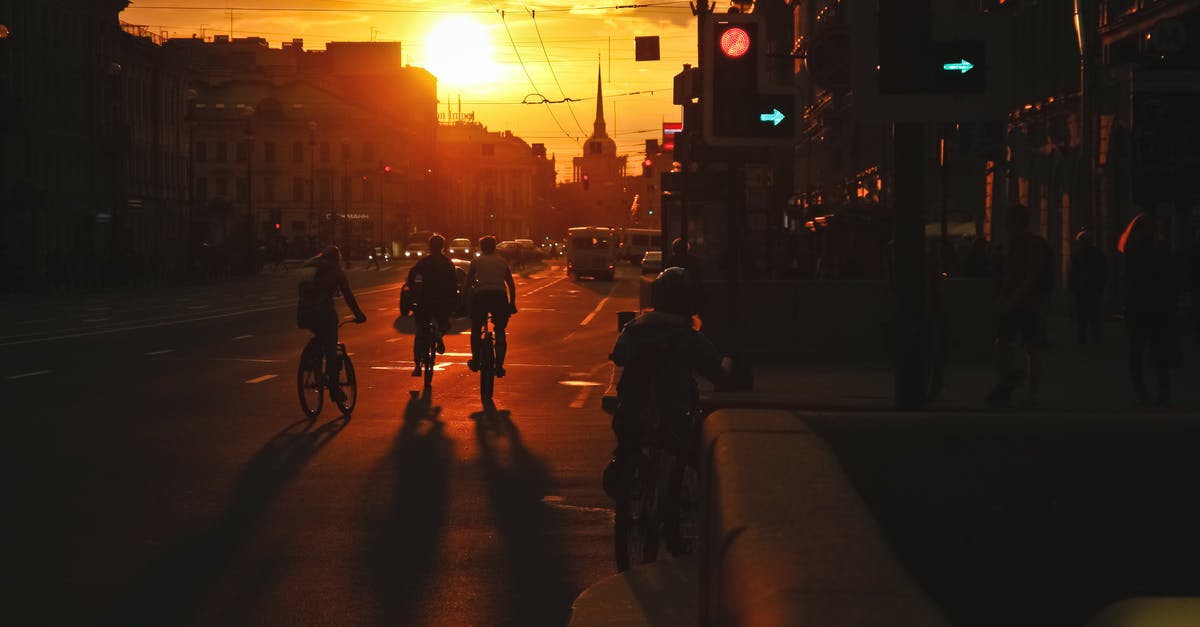 Should I walk facing traffic when walking on a bike trail? - Busy street with vehicles driving along asphalt road and pedestrians walking on sidewalk in evening at sundown