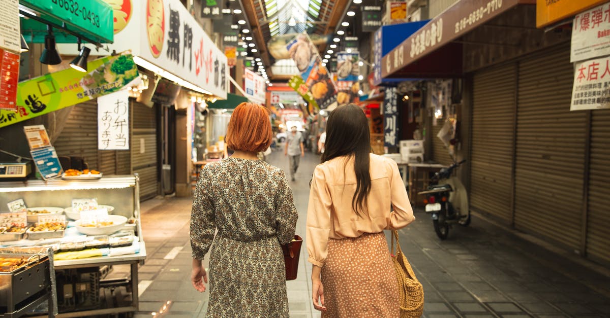 Showing tax-refunded items at Customs in Japan - Back view of unrecognizable trendy female travelers in stylish clothes walking in traditional famous Nishiki Market in Kyoto